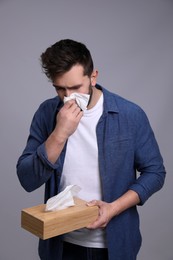 Man sneezing on grey background. Cold symptoms
