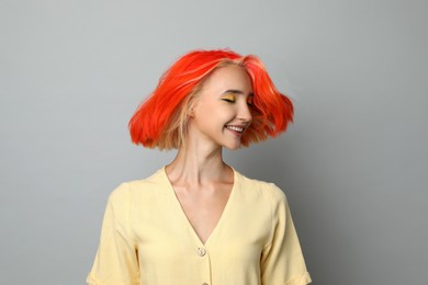 Beautiful young woman with bright dyed hair shaking head on light grey background