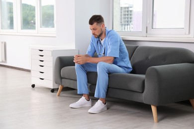 Photo of Exhausted doctor sitting on sofa in hospital