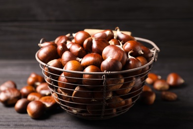 Photo of Fresh sweet edible chestnuts in basket on black table, closeup