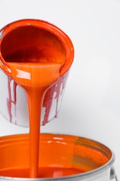 Pouring orange paint from can on white background