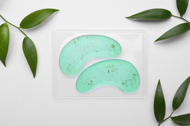 Package with under eye patches and green twigs on white background, flat lay. Cosmetic product