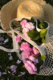 Photo of Straw hat and mesh bag with beautiful tea roses on green grass outdoors