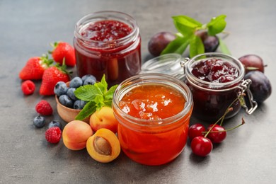 Jars with different jams and fresh fruits on grey table