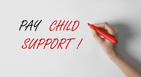 Woman writing phrase PAY CHILD SUPPORT! on white background, closeup