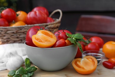 Different sorts of tomatoes with basil on wooden table