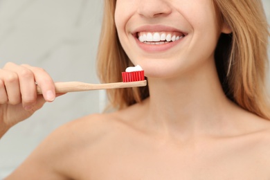 Woman holding brush with toothpaste indoors, closeup
