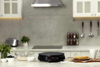 Photo of Electric crepe maker and ingredients on white marble table in kitchen