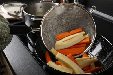 Photo of Woman putting cut parsnips and carrots into wok pan in kitchen, closeup