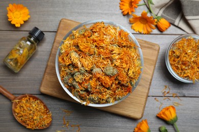 Dry calendula flowers and bottle with tincture on wooden table, flat lay