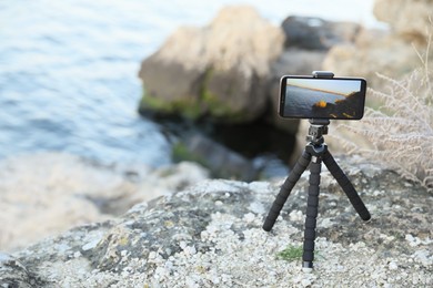 Tripod with smartphone on rocky river coast. Space for text
