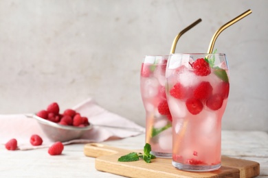 Glasses of refreshing drink with raspberry and mint on white wooden table against grey background, space for text