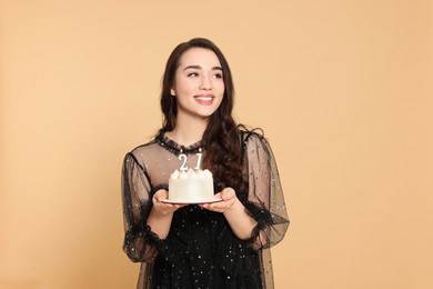 Photo of Coming of age party - 21st birthday. Smiling woman holding delicious cake with number shaped candles on beige background