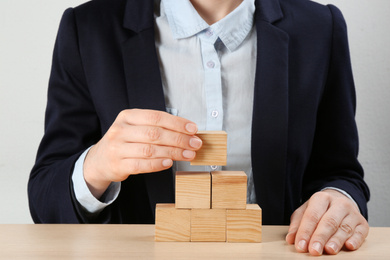 Photo of Woman building pyramid at wooden table, closeup. Career promotion concept