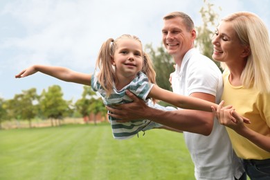 Cute little girl having fun with her parents in park on summer day