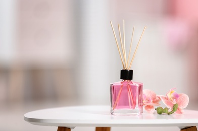 Aromatic reed air freshener and flowers on table against blurred background