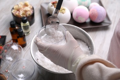 Woman in gloves making bath bomb at wooden table, closeup