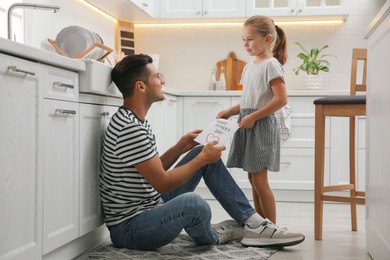 Photo of Little girl greeting her dad with Father's Day in kitchen