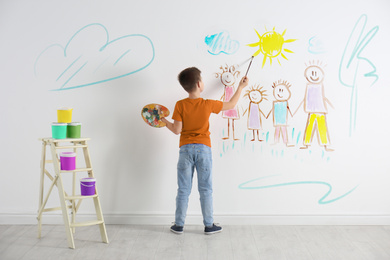 Little child drawing family on white wall indoors