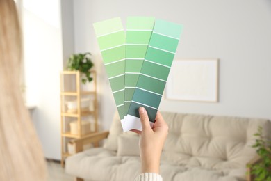Photo of Woman choosing color for wall in room, focus on hand with paint chips. Interior design