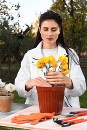 Photo of Woman transplanting flowers into pot at table outdoors