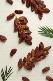 Sweet dried dates and green leaves on white wooden table, flat lay