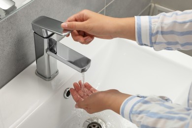Woman washing hands with water from tap in bathroom, closeup