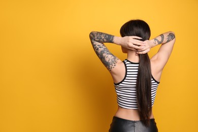 Beautiful woman with tattoos on arms against yellow background, back view. Space for text