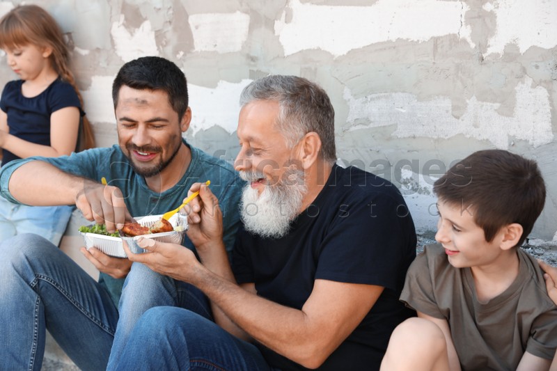 Poor people holding plates with food near wall outdoors