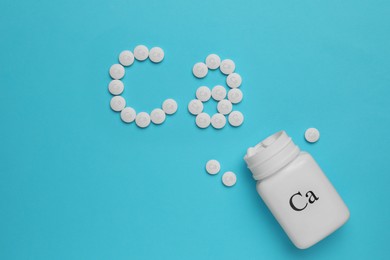 Flat lay composition with calcium supplement pills on light blue background, space for text