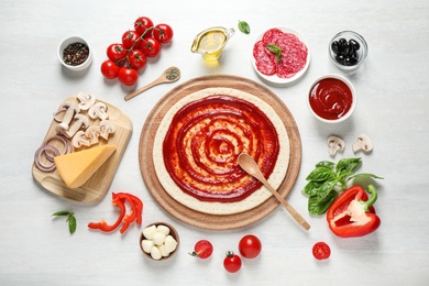 Flat lay composition with pizza crust and ingredients on white wooden table