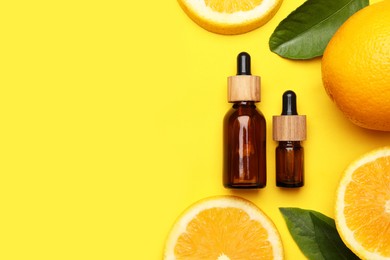 Bottles of citrus essential oil and fresh oranges on yellow background, flat lay. Space for text