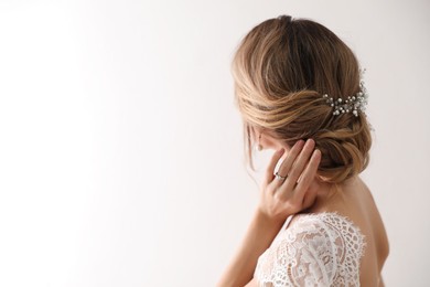 Young bride with elegant wedding hairstyle on light background, back view. Space for text