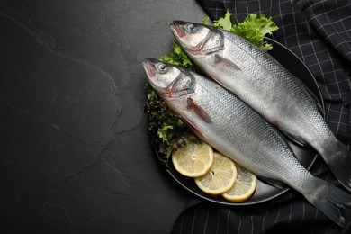 Photo of Fresh raw sea bass fish and ingredients on black table, top view. Space for text