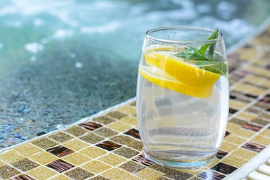 Refreshing water with lemon and mint on edge of swimming pool, space for text