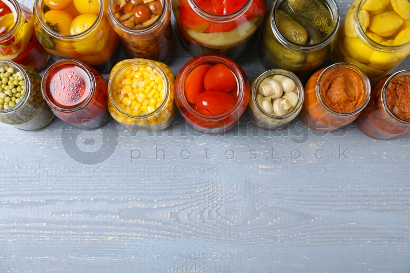 Jars of pickled vegetables on light wooden table, flat lay. Space for text