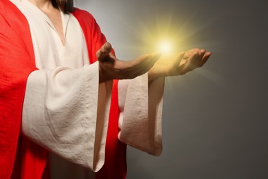 Jesus Christ on grey background, closeup. Miraculous light in hands