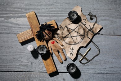 Female voodoo doll with heart and ceremonial items on grey wooden table, flat lay