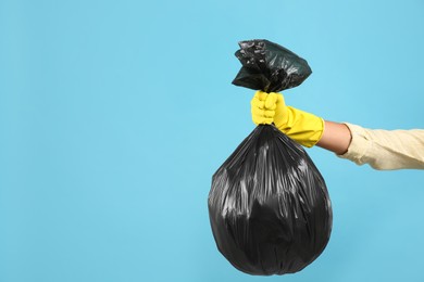 Woman holding full garbage bag on light blue background, closeup. Space for text