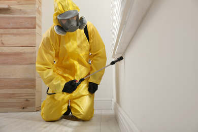 Pest control worker in protective suit spraying insecticide on window sill at home