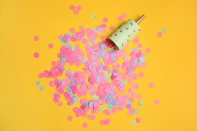 Photo of Party popper with bright confetti on orange background, flat lay