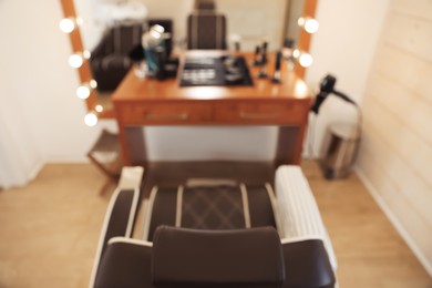 Photo of Blurred view of stylish hairdresser's workplace with armchair and professional tools in barbershop