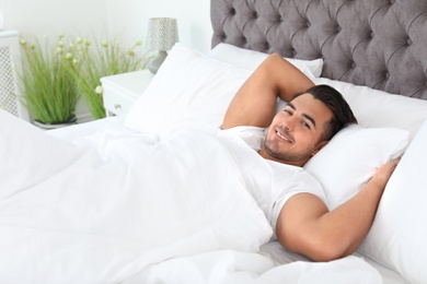 Young man lying in bed with soft pillows at home