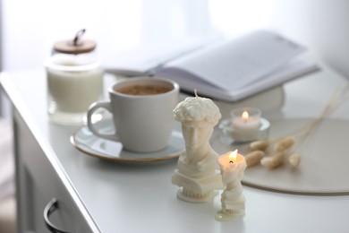 Beautiful David bust candles and cup of hot drink on  white table indoors, space for text
