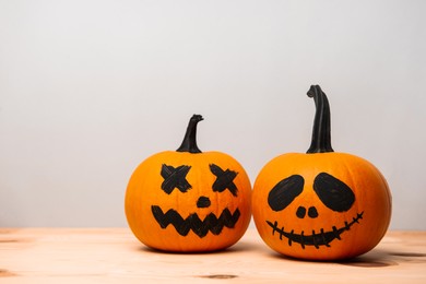 Halloween celebration. Pumpkins with drawn faces on wooden table against light grey background, space for text