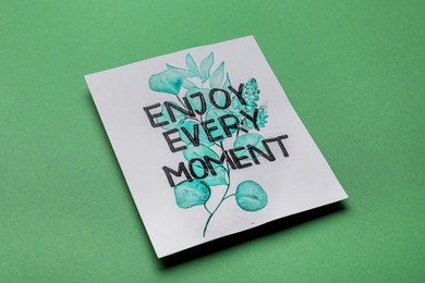 Photo of Card with phrase Enjoy Every Moment on green background