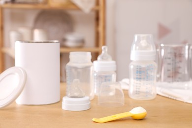 Scoop with powdered infant formula, can and bottles on wooden table indoors. Baby milk