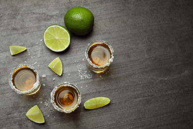 Mexican Tequila shots, lime slices and salt on grey table, flat lay. Space for text