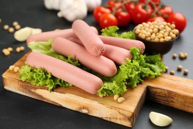 Fresh raw vegetarian sausages and vegetables on black table, closeup