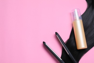 Photo of Spray bottle with thermal protection, iron and lock of black hair on pink background, flat lay. Space for text